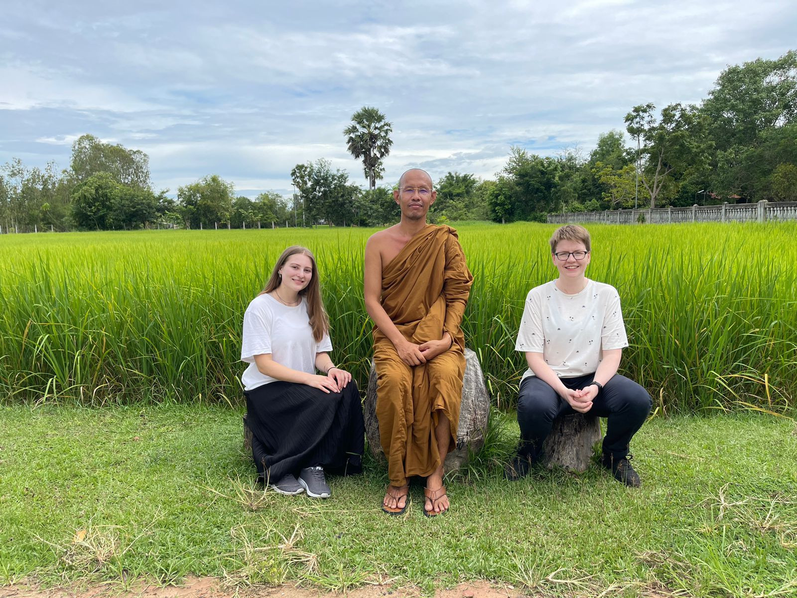 Drei Menschen sitzen auf einem Stein vor hochgewachsenem Gras.