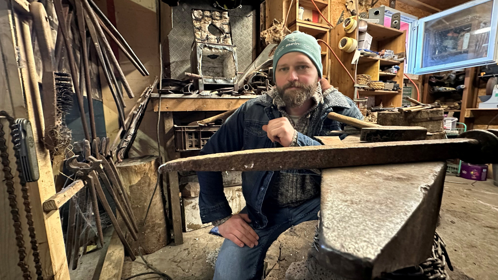 Person in Werkstatt mit Amboss, Hammer und verschiedenen Schmiedewerkzeugen